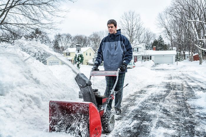 A person operates a snowblower to clear a snow-covered driveway