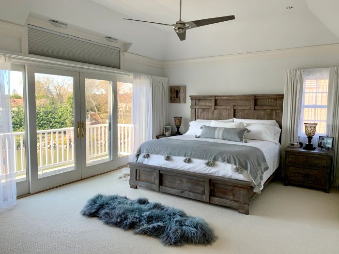 A spacious, well-lit bedroom featuring a large cozy bed, wooden furnishings, soft carpeting, and elegant balcony doors letting in natural light.