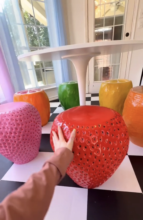 A person reaching for a large red strawberry chair at the table, surrounded by other vibrant fruit-themed chairs