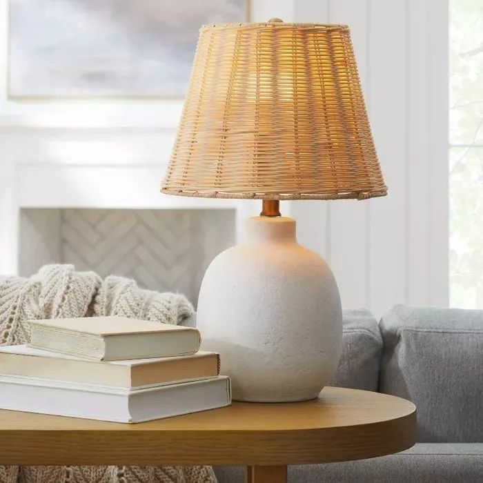 A woven rattan lampshade atop a ceramic base, placed beside stacked books on a wooden table