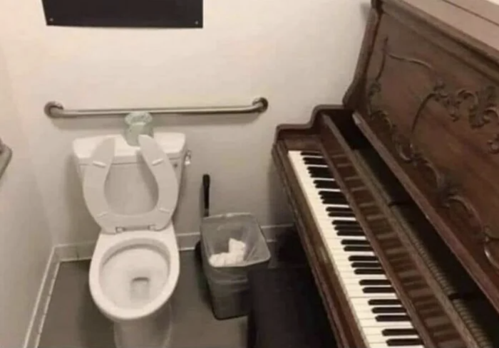 A bathroom with a toilet positioned next to an upright piano, creating a quirky and amusing combination in a tight space