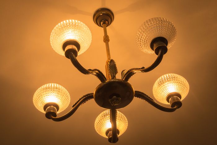 A classic chandelier featuring five illuminated glass globes and intricate brass arms; the chandelier is affixed to the ceiling, casting a warm, inviting light across the room.