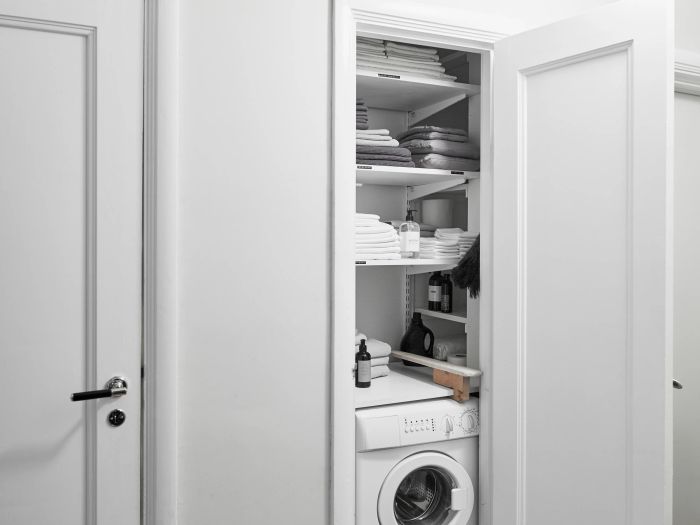 A neatly organized open closet featuring shelves stocked with towels and a washing machine tucked in for convenience.