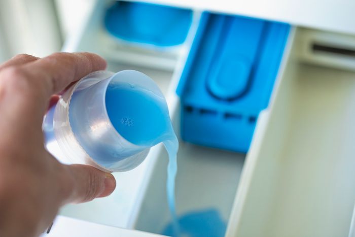 Person pouring liquid detergent into the washing machine’s dispenser drawer