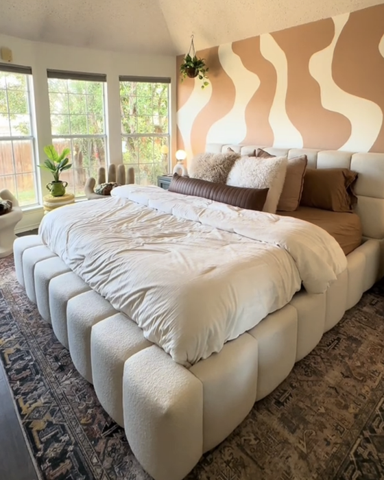 A cozy bedroom with a large bed adorned with pillows, a patterned wall, a ceiling fan, and large windows letting in natural light