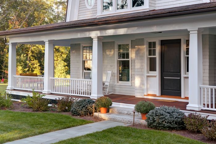 A charming house with a front porch featuring columns, a rocking chair, potted plants, and a well-maintained lawn.