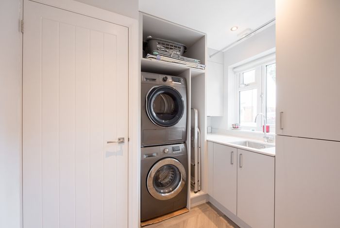 A contemporary laundry room equipped with a stacked washer and dryer, surrounding cabinets, a folding station with a laundry basket, and a sink placed next to a window.