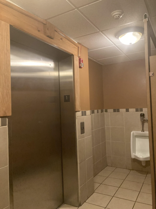 An elevator that opens directly into a bathroom beside a urinal