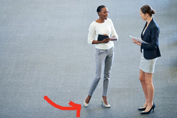 Two professionals having a conversation, one holding a tablet. An arrow highlights the one standing with one foot raised