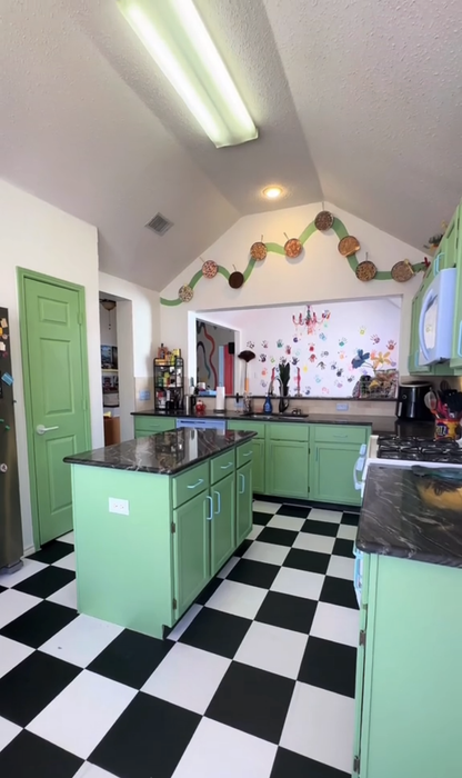 A kitchen with a checkered floor, green cabinets, and various decorative items displayed on walls and shelves