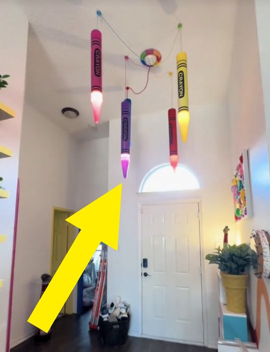 A room with crayon-shaped lights, eclectic decor, and a skateboard near the entrance