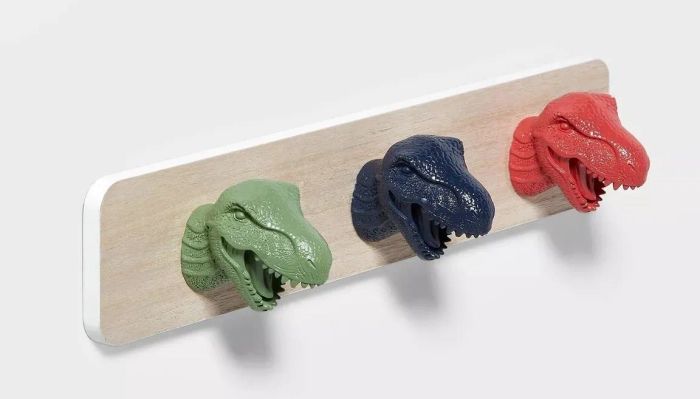 A wooden rack featuring three dinosaur head-shaped hooks in green, blue, and red — a fun way to keep your items organized.