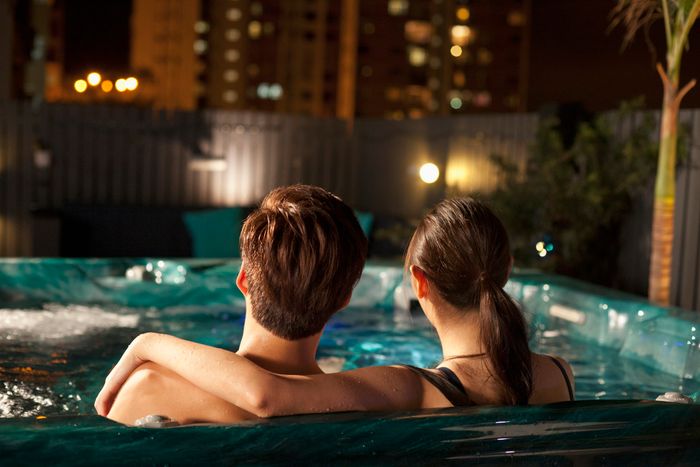 Two people enjoying a hot tub with city lights in the background at night