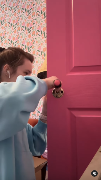 Kaarin is seen installing a new doorknob on a vibrant pink door in her home