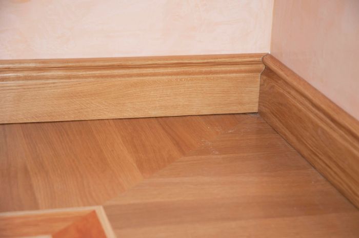A wooden baseboard seamlessly joining a laminate floor at the corner of a cozy room.