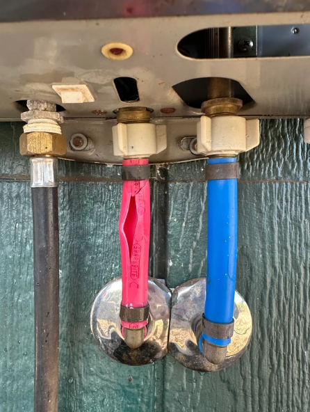 Pipes with red and blue handles for hot and cold water, set against a green wall.