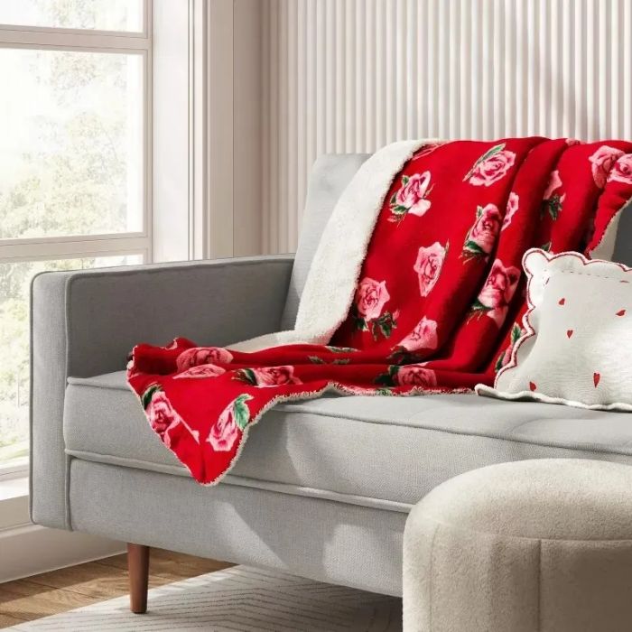 A sofa with a red floral-patterned blanket draped over it and a matching decorative pillow.