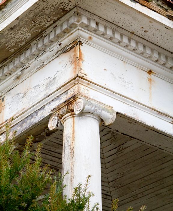 Close-up of a worn white classical column with an ornate capital, part of an aging building's architecture.