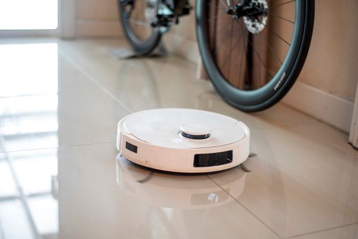 A robotic vacuum sweeps the tile floor with a bike hanging on the wall in the background