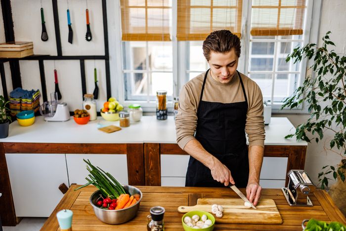 A man in an apron slicing vegetables on the kitchen counter, preparing a meal