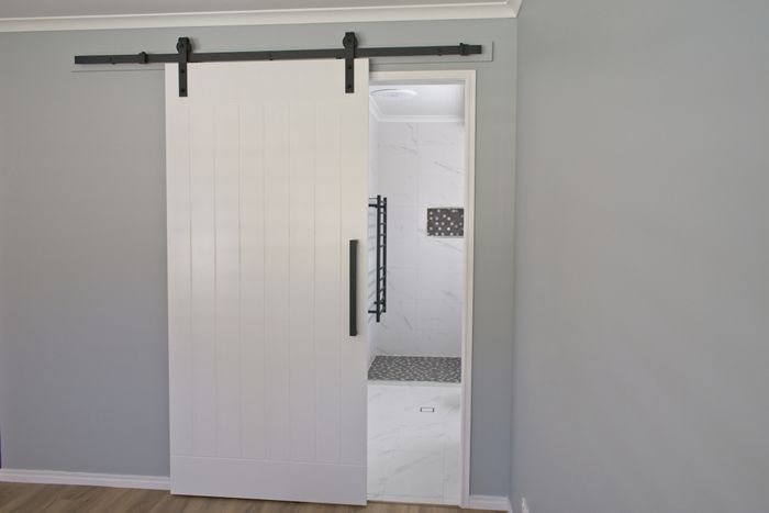 A modern interior featuring a white sliding barn door slightly open, unveiling a clean and minimalist bathroom space.