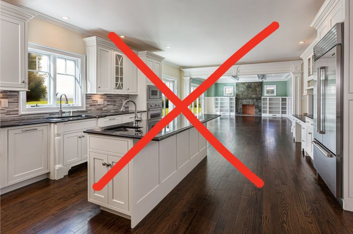 A spacious, modern kitchen featuring white cabinets, stainless steel appliances, dark hardwood floors, an island, and a clear view of a living area with a fireplace.