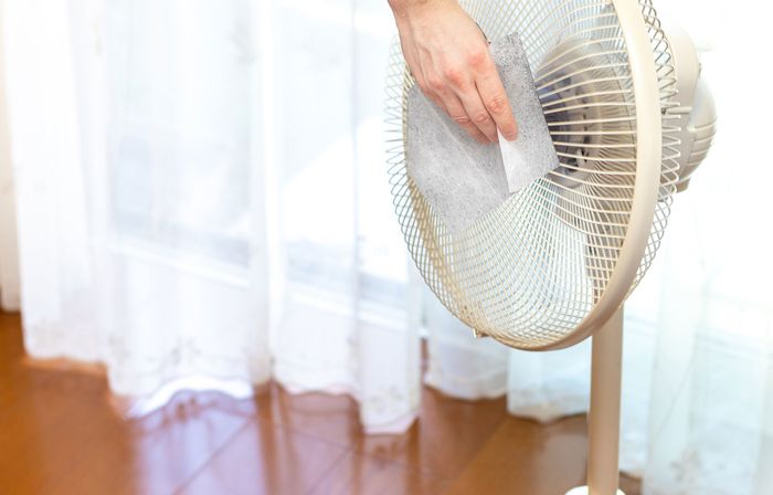 Person attaching a filter behind a fan in a room