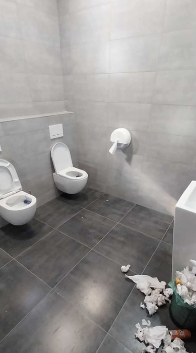 A bathroom with two toilets positioned so that only one person can reach the toilet paper