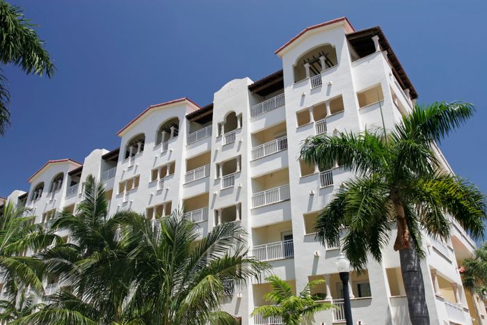 A bright view of a multi-story residential building with a white facade and red accents, framed by palm trees.
