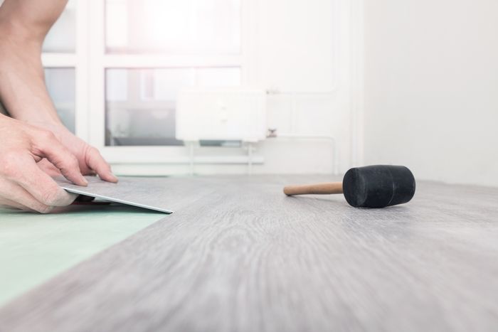 Hand installing new laminated wooden flooring with a rubber mallet nearby