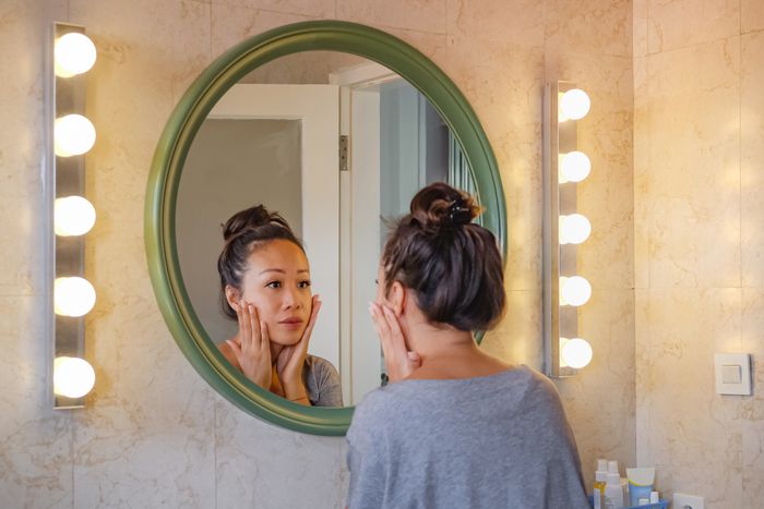 Woman inspecting her skin in a well-lit bathroom mirror, focusing on skincare