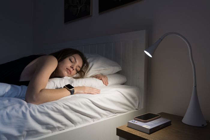 Woman resting in bed with a book and a bedside lamp glowing softly