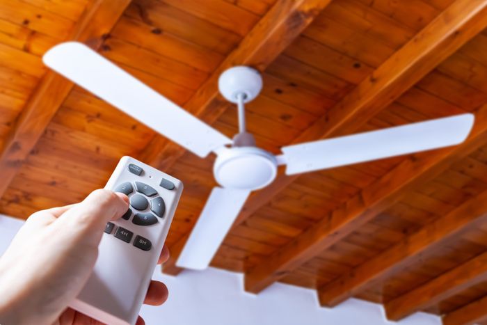 A person controlling a ceiling fan with a remote, with wooden beams visible overhead