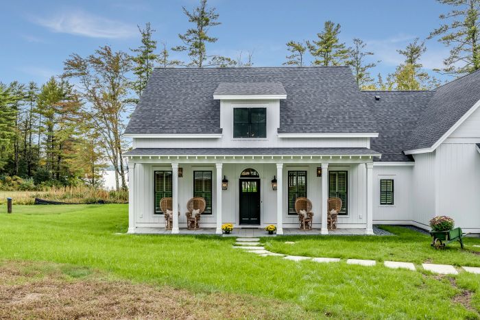 A charming white home with a sleek black roof, a cozy front porch featuring inviting chairs, and a beautifully maintained lawn.