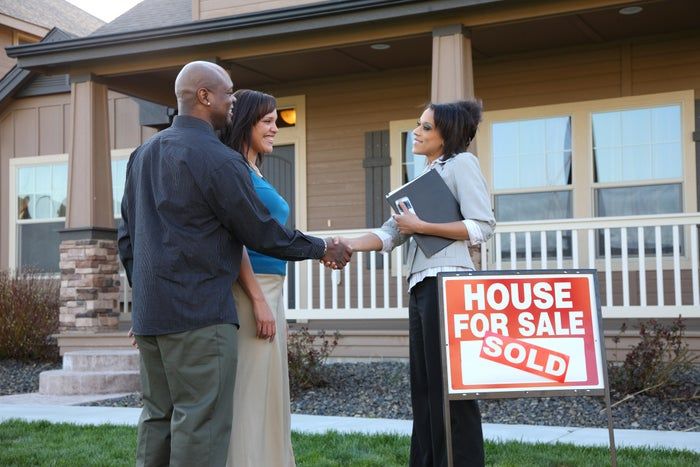 A realtor exchanging a handshake with a couple who have just closed on their new home.