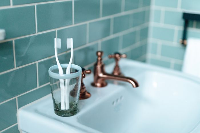 Two toothbrushes resting in a glass cup on a bathroom sink with stylish bronze faucet fixtures.