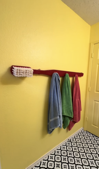 An oversized toothbrush on the wall doubling as a towel hanger in a quirky home environment