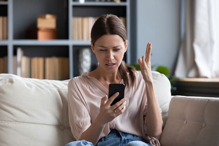 A woman staring at her phone with her hand raised in frustration.