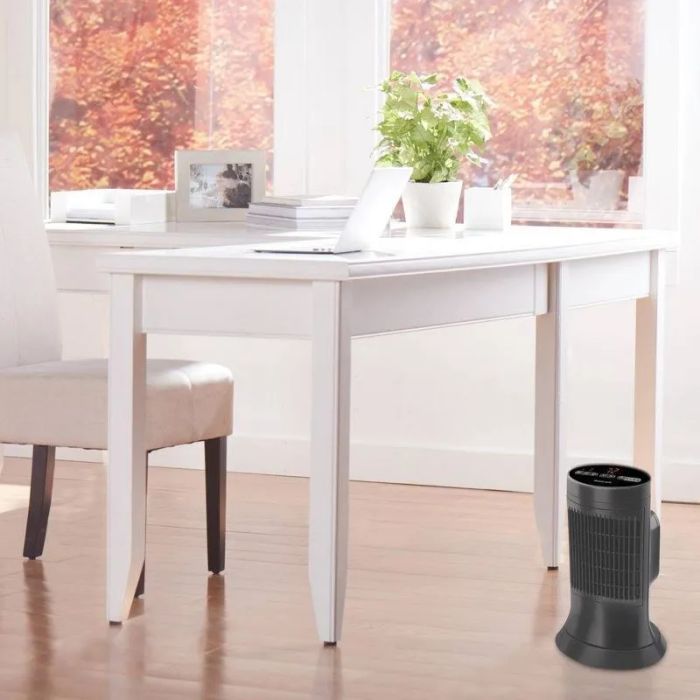 A sleek, compact air purifier placed on the floor next to a minimalist white desk adorned with decorative plants