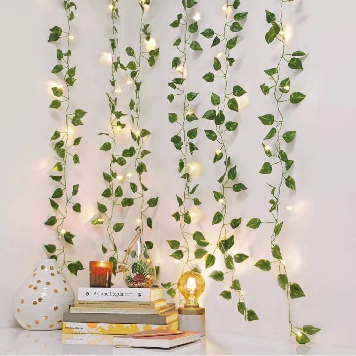 A string of lights entwined with artificial ivy, cascading down a wall near stacked books and a lit bulb.