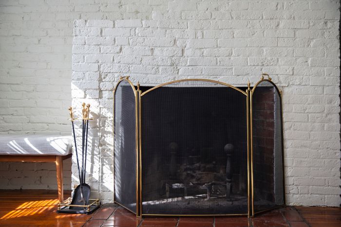 A fireplace with a mesh screen and tools placed against a white brick wall, next to a wooden bench