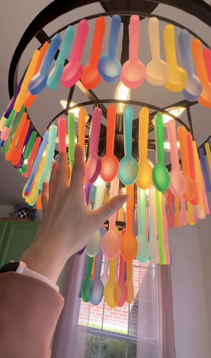 A hand reaching for a vibrant chandelier made of hanging utensils in a cozy room