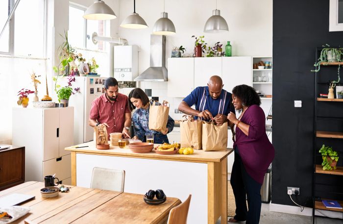 A well-lit kitchen where four people are joyfully unpacking fresh groceries together.