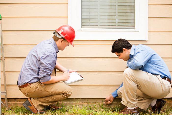 Two men inspecting the foundation of a house.