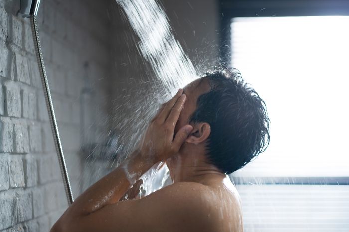 A person showering, facing away, with water cascading over them