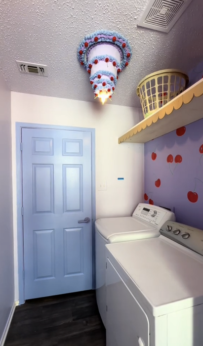 A playful laundry room featuring a cake-themed light fixture, a washer, dryer, and walls adorned with hand-painted cherries