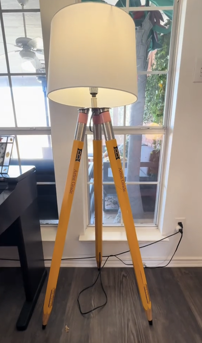 An eccentric lamp with a shade held up by three large pencils, placed next to a window in the room