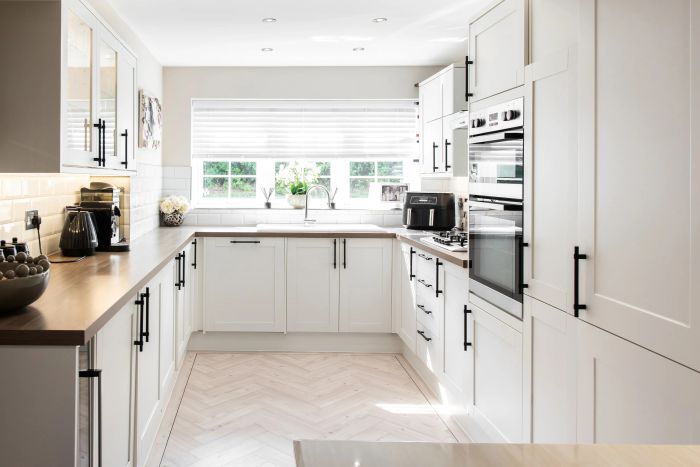 A sleek, modern kitchen featuring crisp white cabinetry, state-of-the-art appliances, and an elegant herringbone-patterned floor.