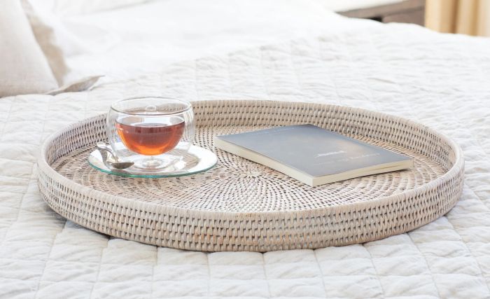 A beautifully woven circular rattan tray elegantly placed on a bed, adding a touch of texture and warmth.