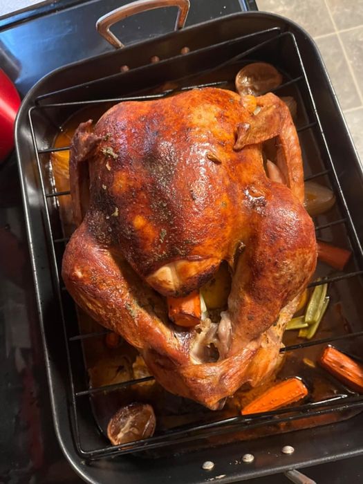 A beautifully roasted turkey in a pan, accompanied by vegetables like carrots and potatoes, perfect for a holiday feast or festive gathering